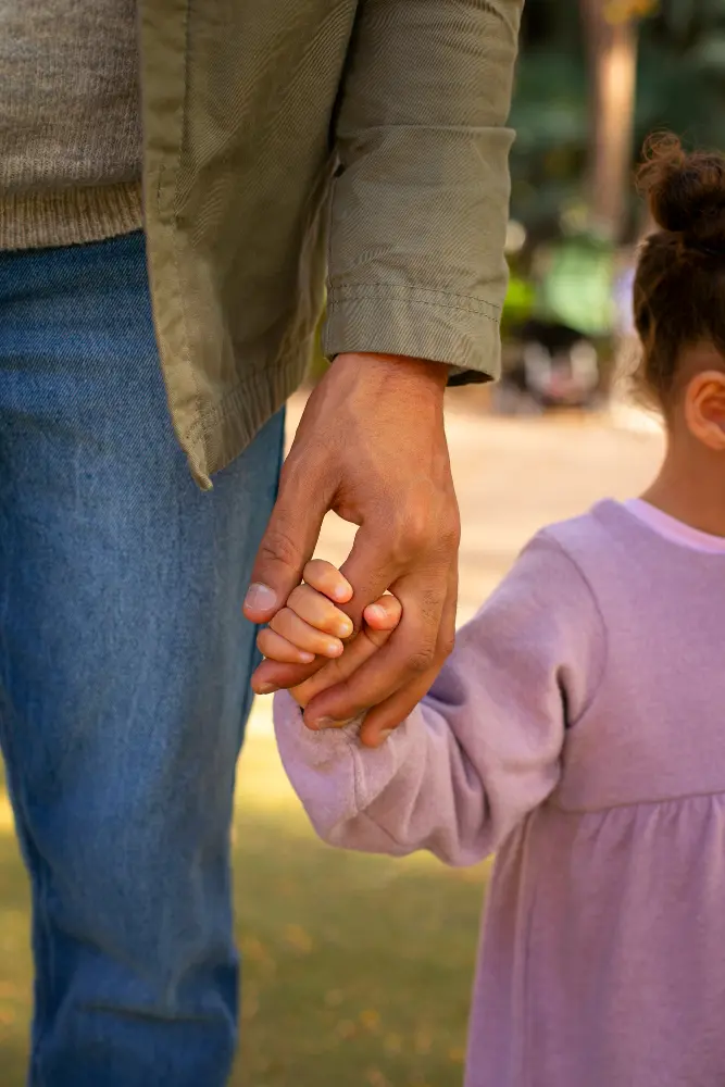 Adulto de mãos dadas com uma criança em um parque, representando a guarda de filhos e a convivência