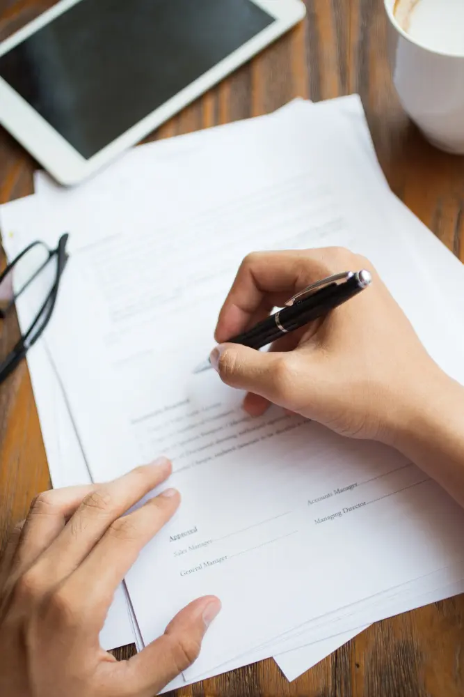 Mão assinando um documento sobre a mesa, representando a elaboração de testamento e planejamento sucessório